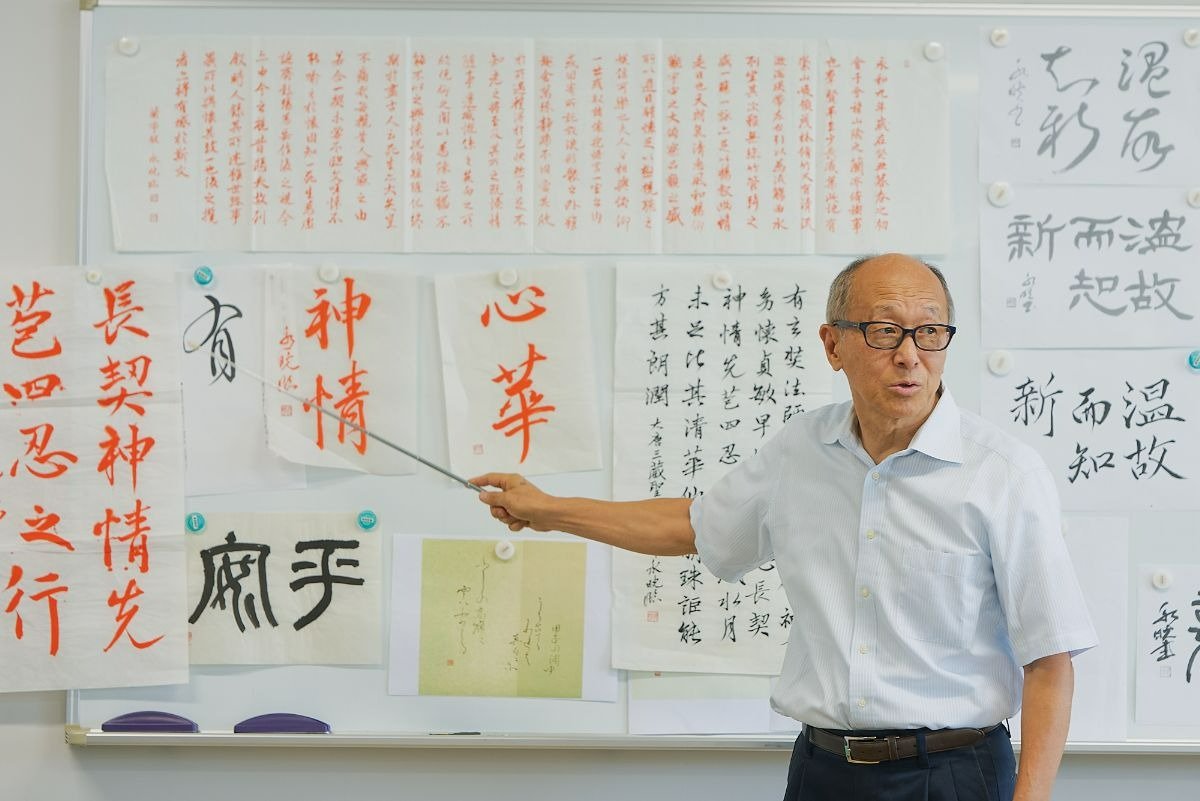 直筆によるいくつものお手本をホワイトボードに貼って解説する若松さん