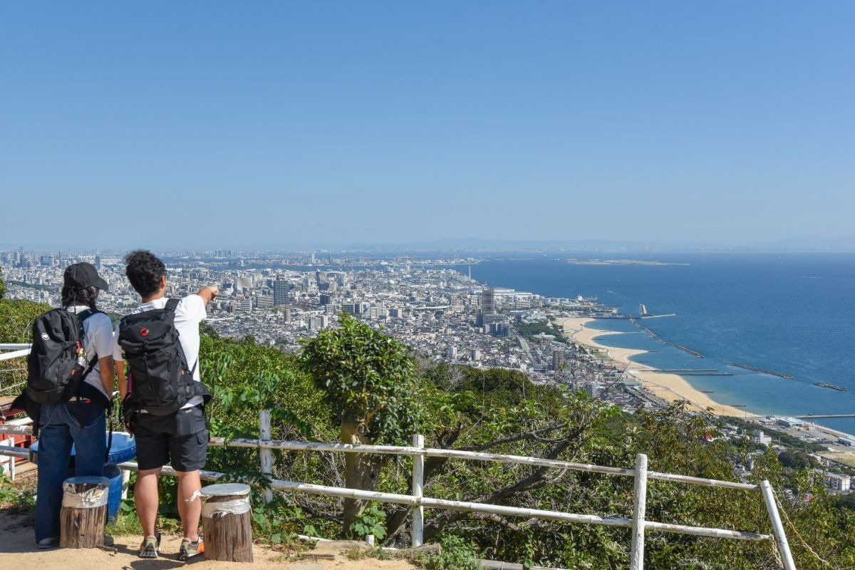旗振山山頂から大阪湾や市街地を一望している男女。男性が海を指さしている。